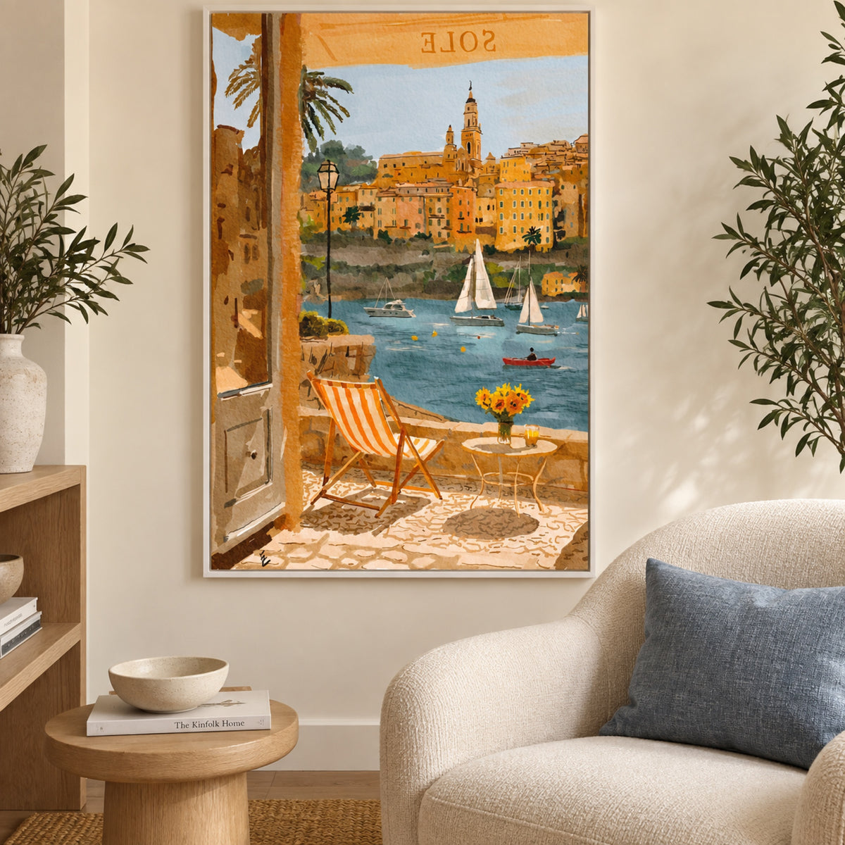 July in menton in a slim white frame beside a cream reading chair, with a blue cushion and pale oak furniture.