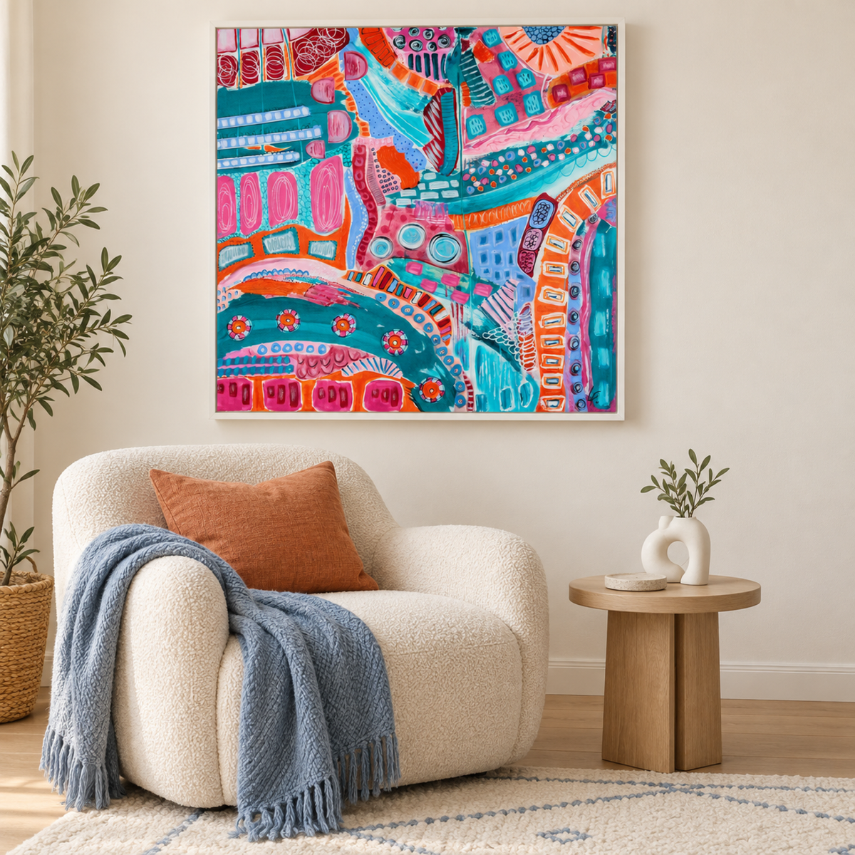 Metropolis by Lindy Farley in a white frame above a cream chair with orange and blue textiles.