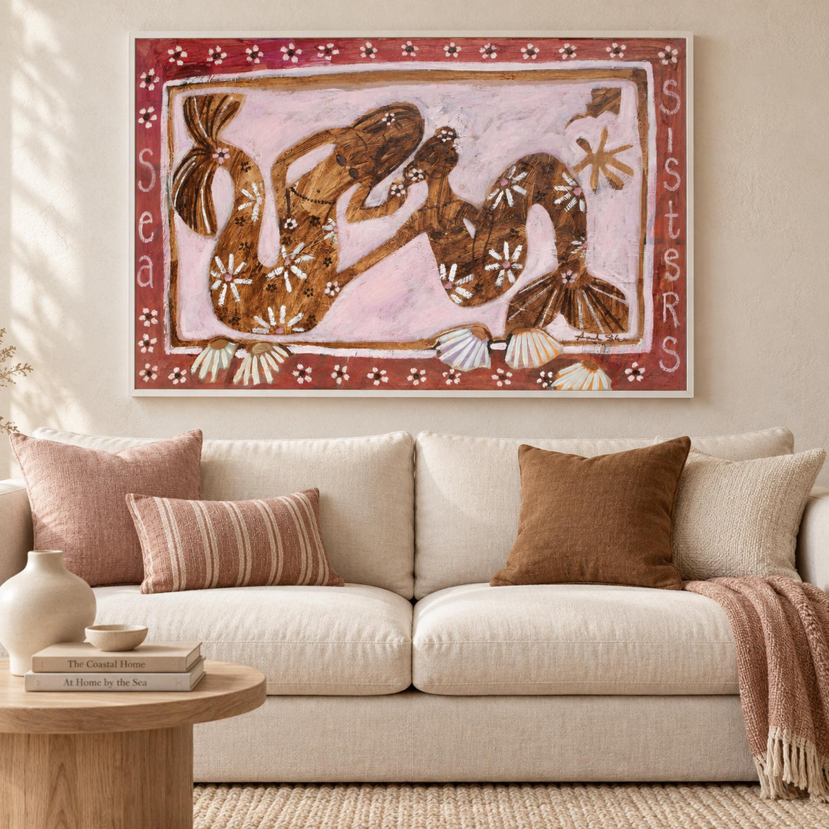 Sea Sisters by Amanda Skye in a white floating frame above a cream sofa with blush and tobacco cushions.