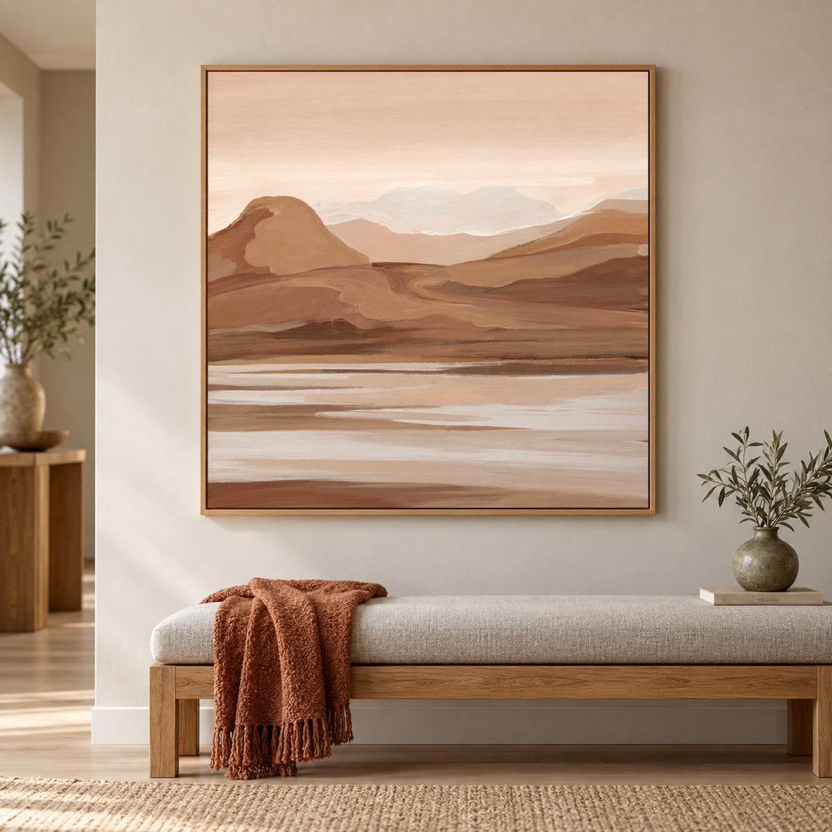 Dunes landscape artwork in an oak frame above a light upholstered bench with a rust throw and olive ceramics.