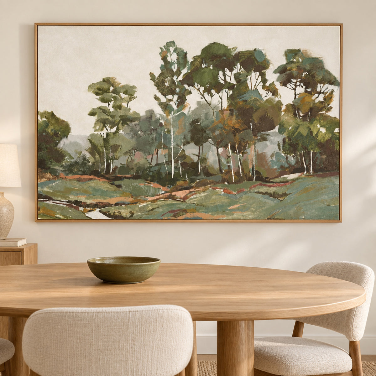 Enchanted Valley in a natural oak frame above an oak dining table with cream chairs and an olive ceramic bowl.