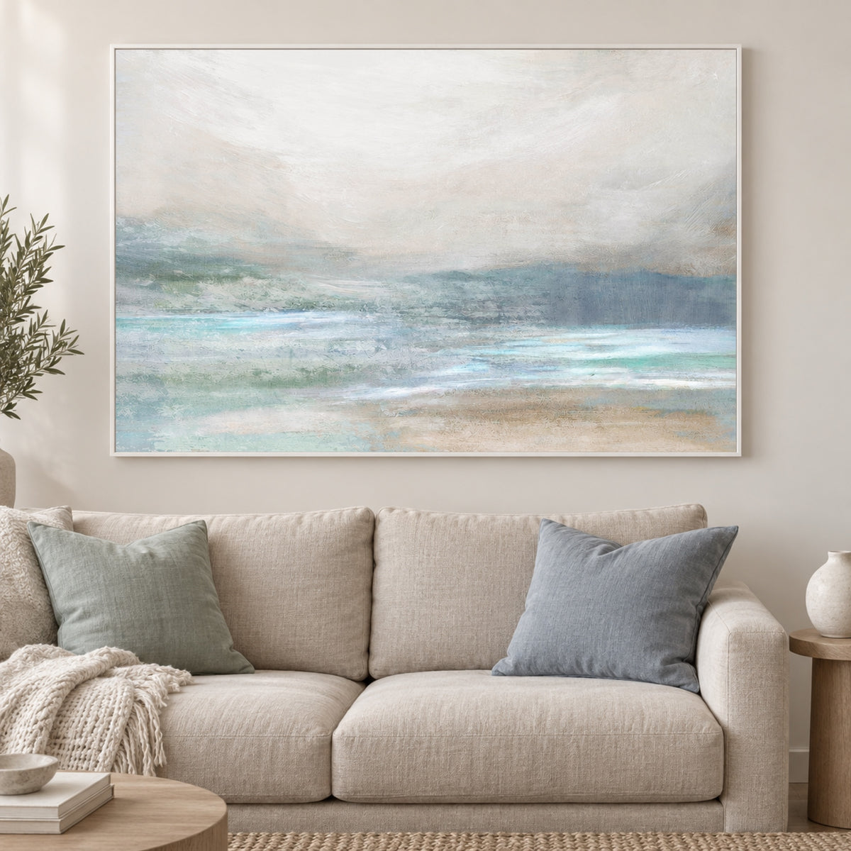 Soft Coastal Mist and Gentle Waves in a slim white frame above a linen sofa with sea-glass and blue cushions.