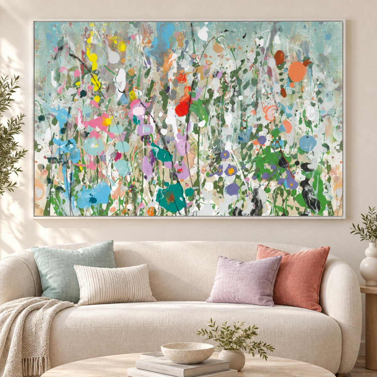 Graffiti Garden by Danhui Nai in a white floating frame above a neutral curved sofa with aqua, lilac and coral cushions.