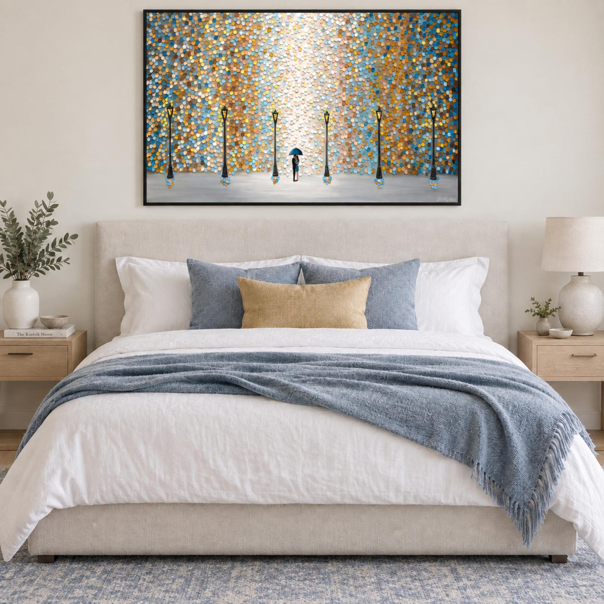 Romance In The Rain in a black frame above a cream bed with blue and gold textiles.